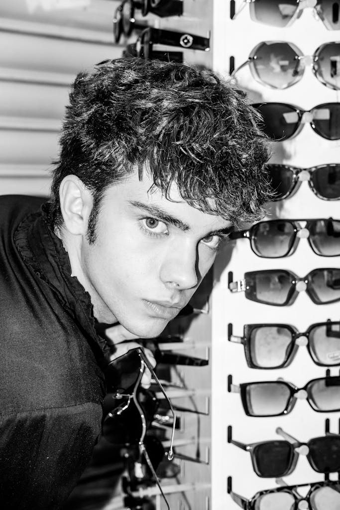 Black and white photo of a man in a store, posing near sunglasses.