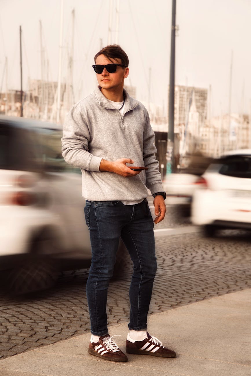 a man in a grey sweater and jeans standing on a street