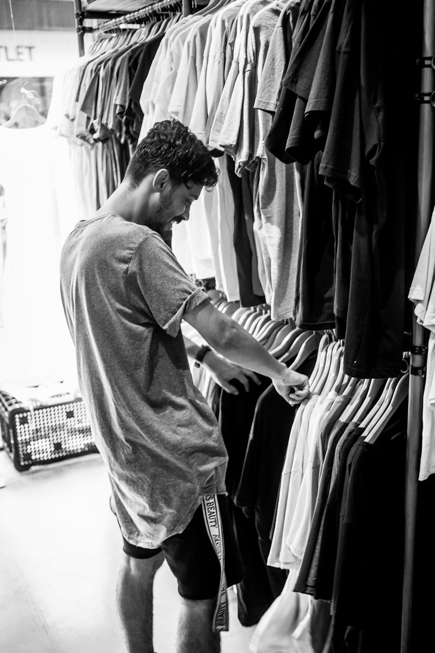 a grayscale of a man looking at clothes on a rack