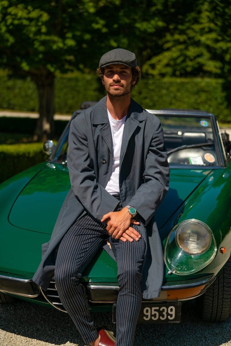 man in gray coat leaning on a green vintage car while looking at the camera